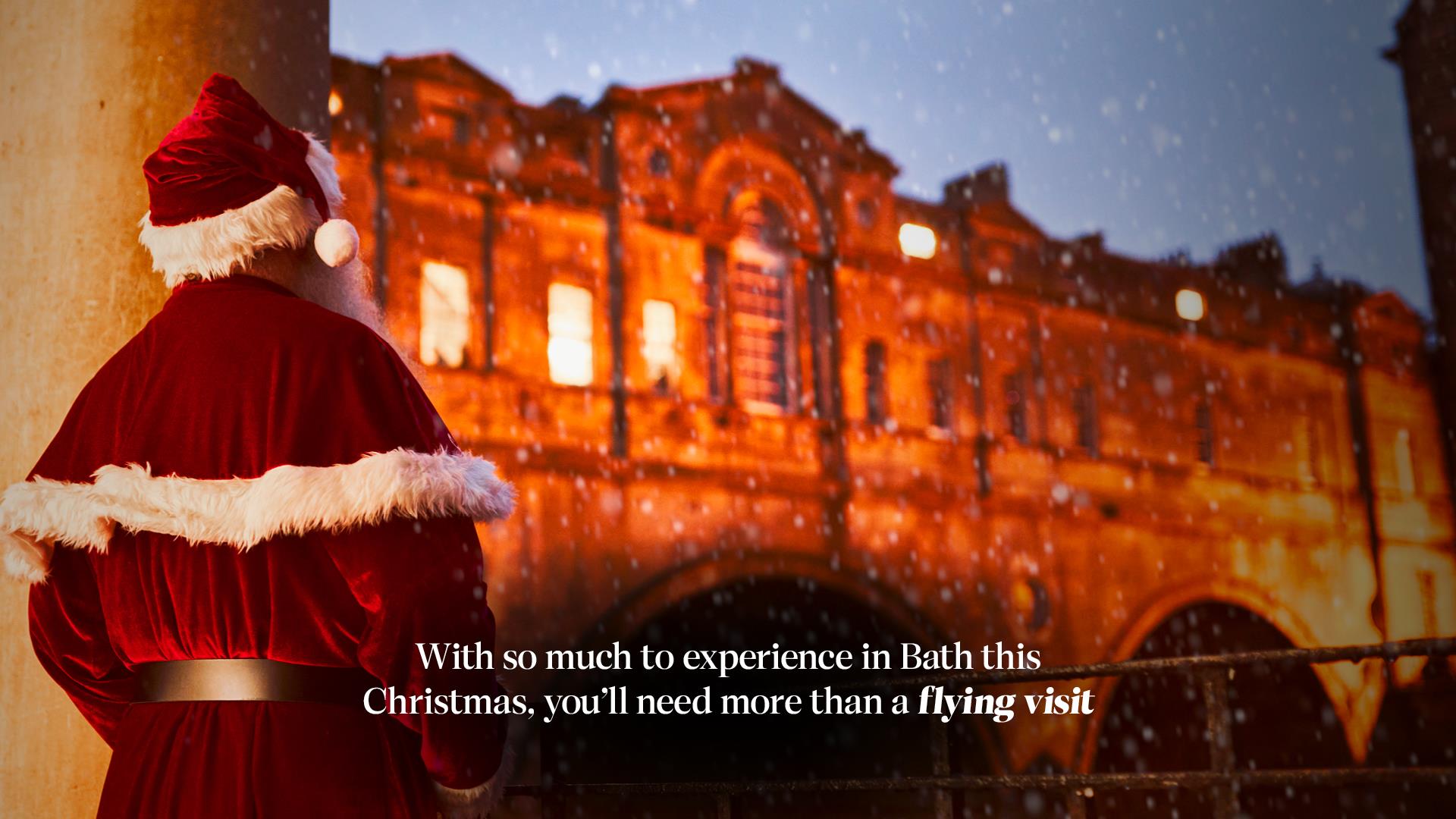 Bath at Christmas Campaign Father Christmas looking at Pulteney Bridge with text overlay