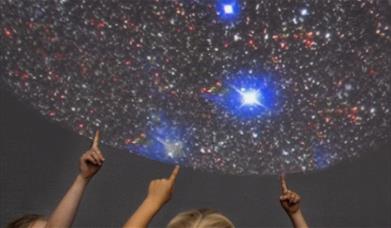 Children's hands pointing at an image of space.