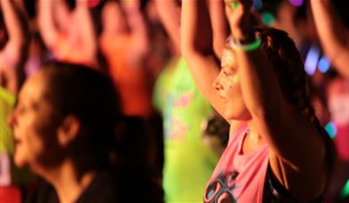 Lots of people in exercise clothes dancing with glow sticks.