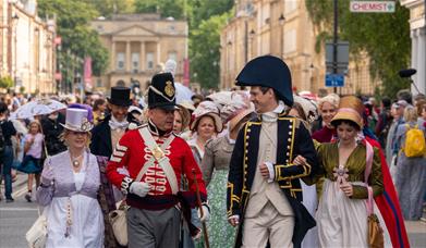 Two men and two women all dressed in Jane Austen-themed costumes leading a procession