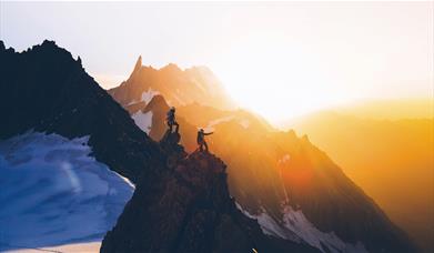 Two people climbing a mountain in the sunrise.