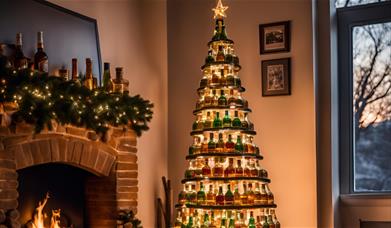 An image of a christmas tree made of whisky bottled in front of a roaring fire. The room is decorated with christmas decorations