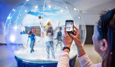 A lady taking a photo of children inside a giant snowglobe