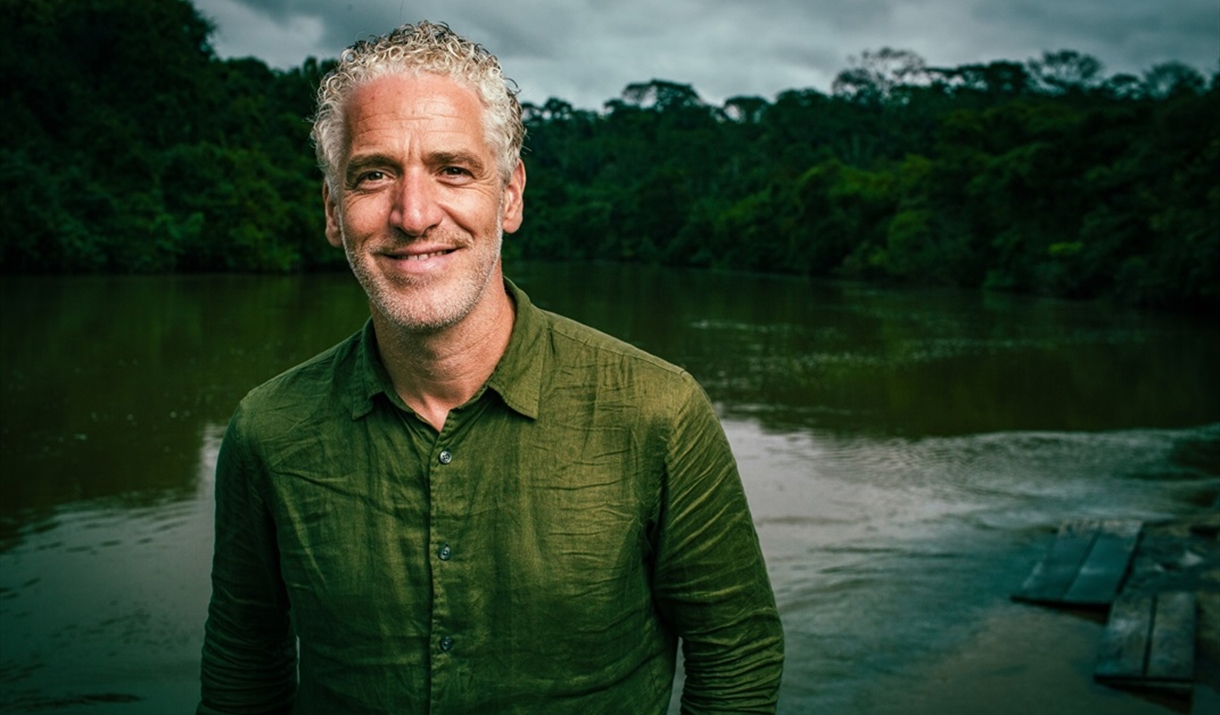 Portrait image of Gordon dressed in a khaki coloured long sleeve shirt, pictured in front of a lake landscape