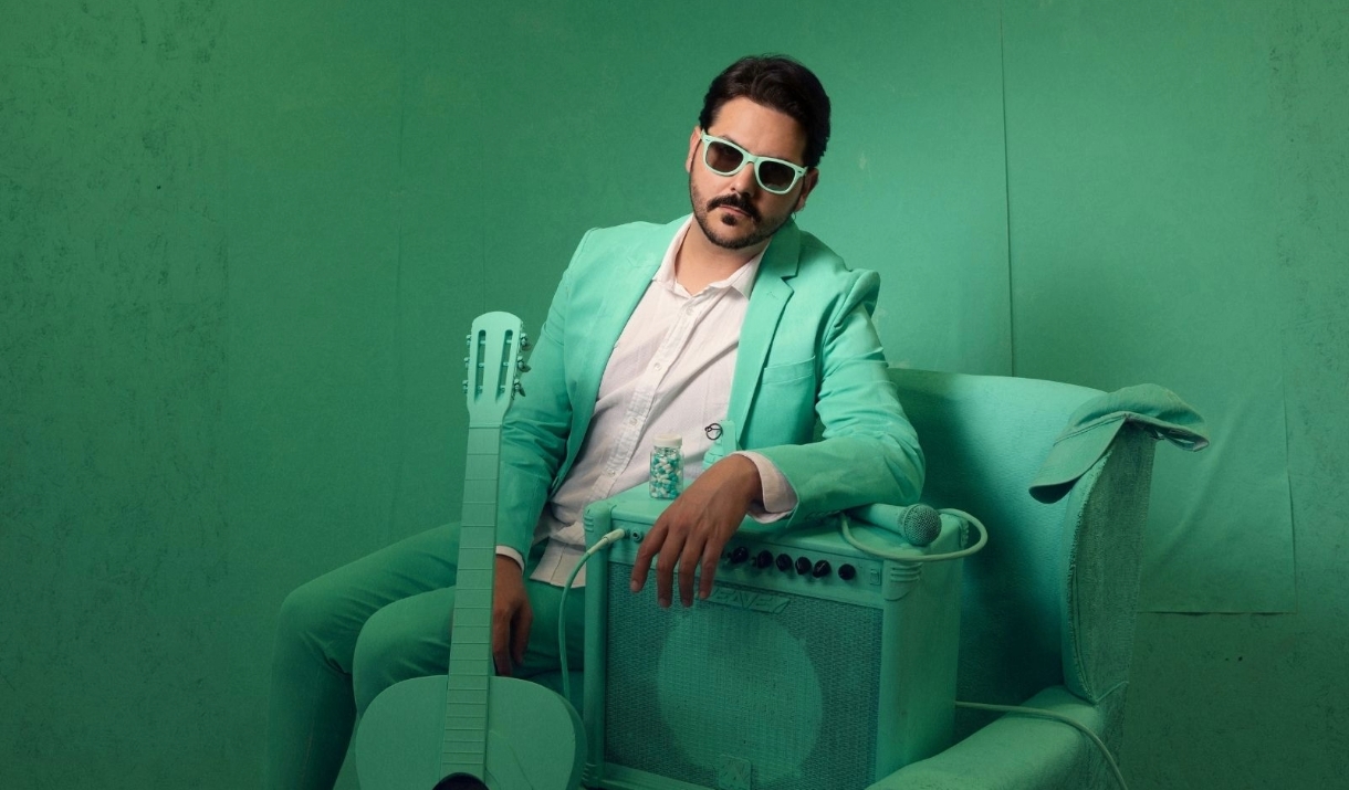 Ignacio Lopez in a turquoise suit in a turquoise room with a turquoise guitar and amplifier