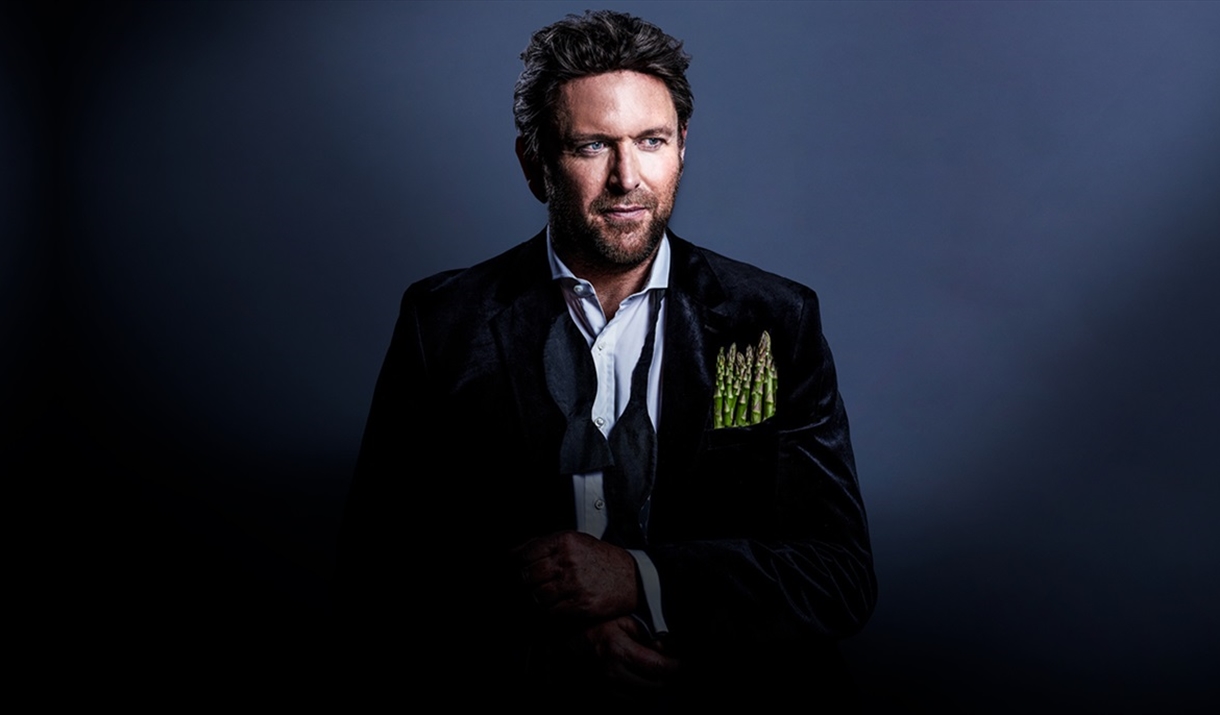 Portrait image of celebrity chef James Martin, wearing a black suit which a handful of asparagus in his jacket pocket.