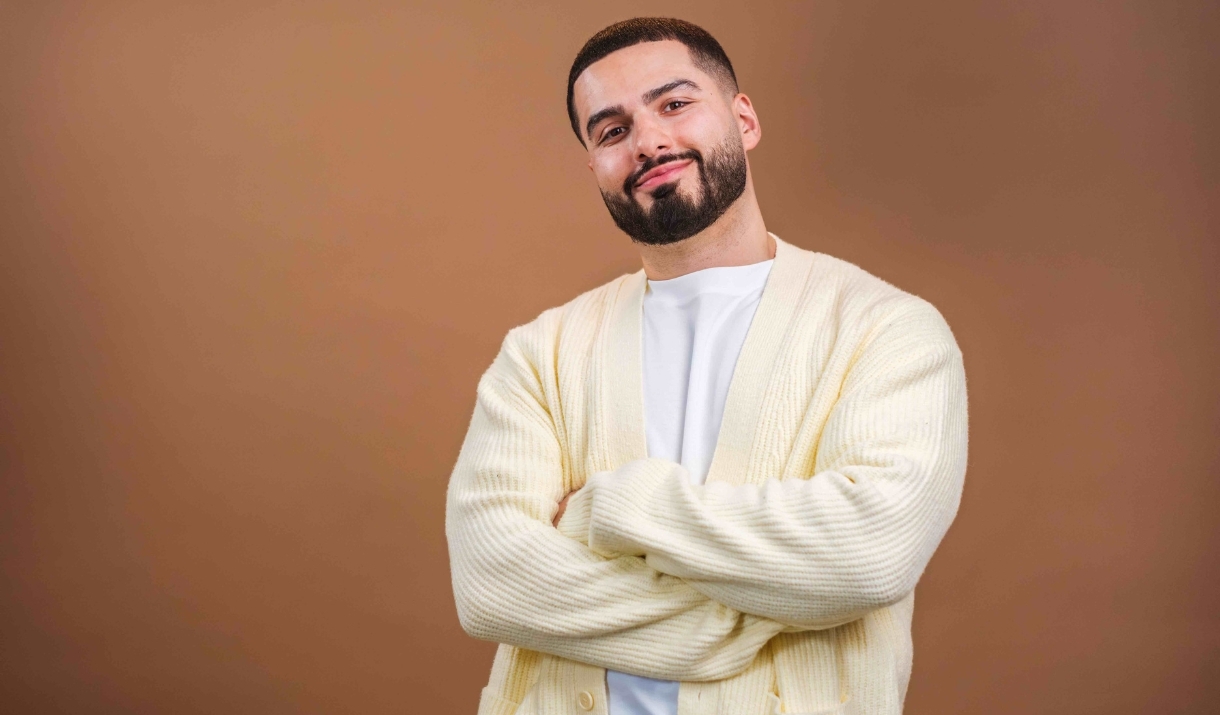 A man smiling with his arms crossed in front of a brown background