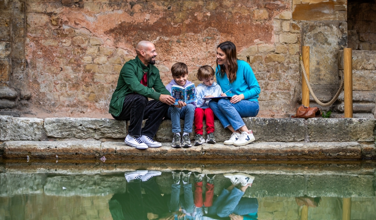 A mother, father and two young sons sitting among some ancient ruins with water in front of them.