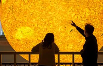 Two people looking closely at Helios at Bath Assembly Rooms