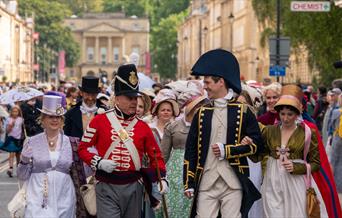 Two men and two women all dressed in Jane Austen-themed costumes leading a procession