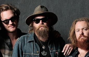 Three men from the band Robert John & The Wreck posing for a photo against a dark background