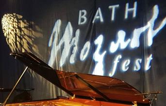 A piano on a stage with the words 'Bath Mozartfest' projected on to a curtain in the background