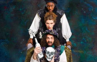 Three members of the cast, holding bottles of wine and the skull of Yorick.