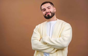 A man smiling with his arms crossed in front of a brown background