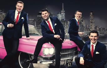 The whole band next to a pink Cadillac