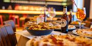 A table full of pizzas and garlic bread with an Aperol spritz  and bottle of beer in the background on a table in the new Upstairs at Bath Pizza Co ba