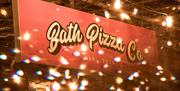 A sign reading "Bath Pizza Co," surrounded by Christmas fairy lights.