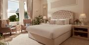 Another photograph of a bed at Bathen House Hotel, this time from an angle and including a couple lounging chairs and a window showing the sun and tre