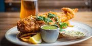 A plate of fish, chips and sauces with a pint of beer in the background at The Scallop Shell in Bath