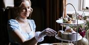 A woman dressed in period costume reaching towards a plate of scones